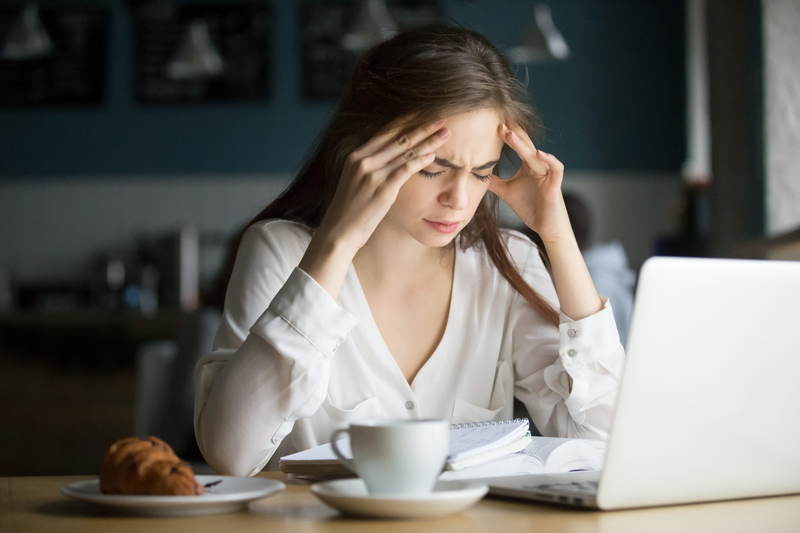 ból głowy w pracy - kobieta siedzi pochylona przed komputerrem i trzyma się za głowę