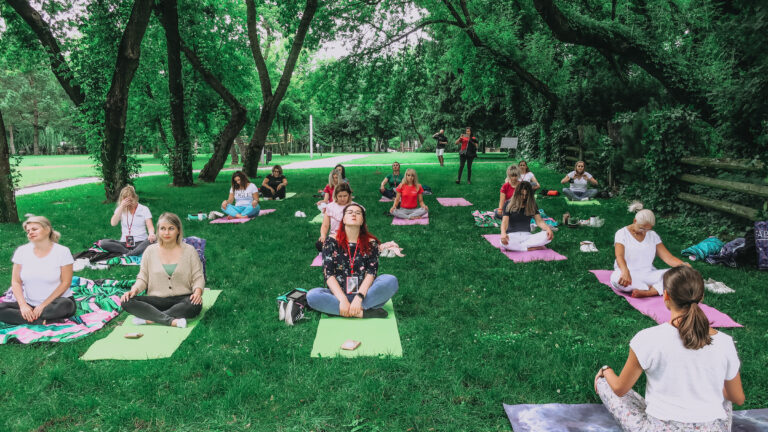 Na matach, na trawie siedzą kobiety i czekają na zajęcia z jogi.