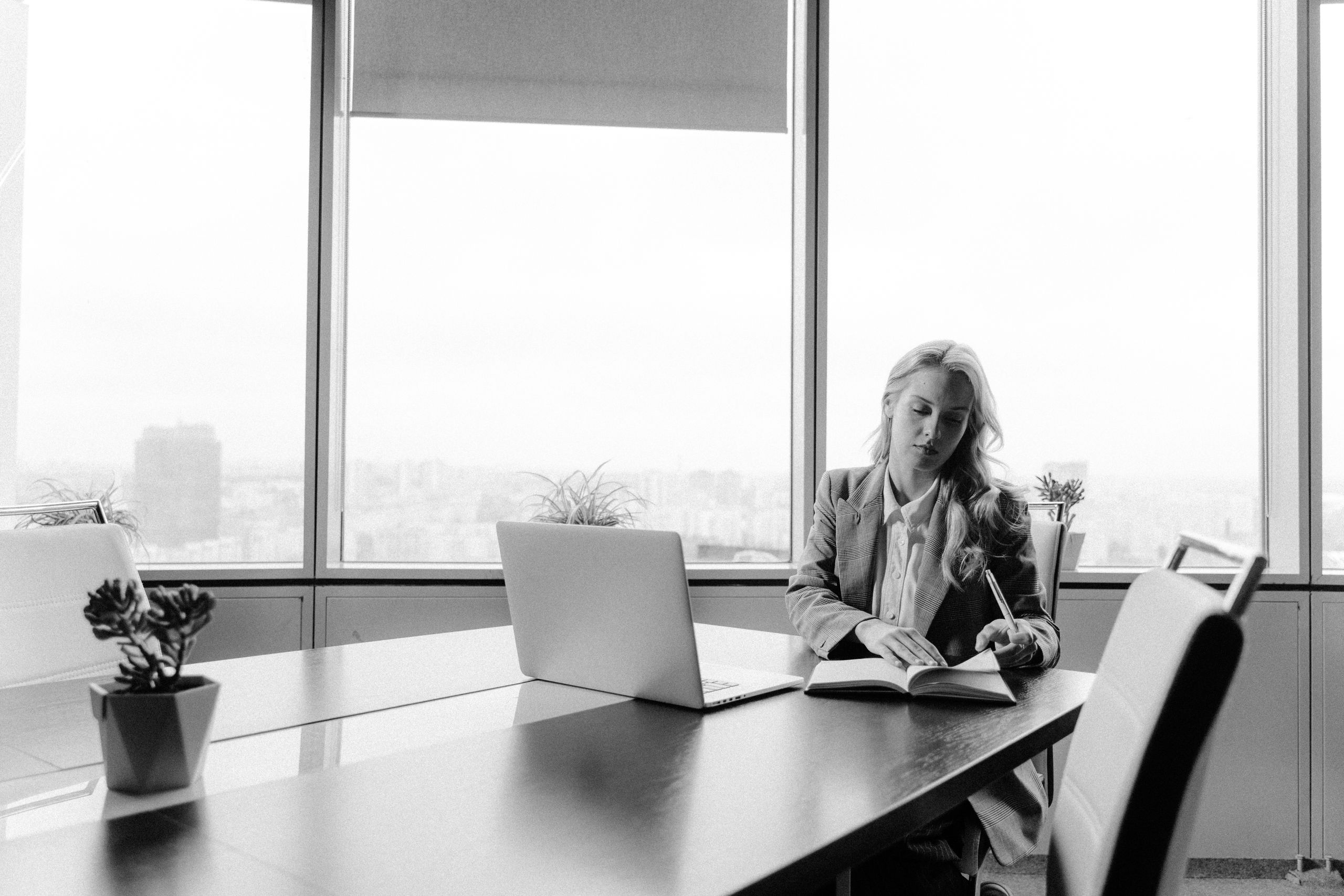 Businesswoman working at a desk in a bright office with city view, in black and white.