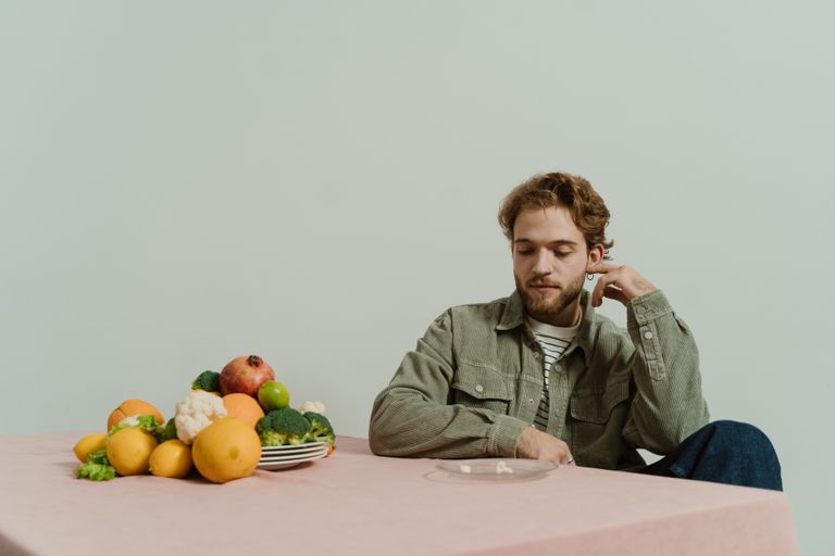 A man in casual attire sits at a table with various vegetables, evoking a thoughtful mood.