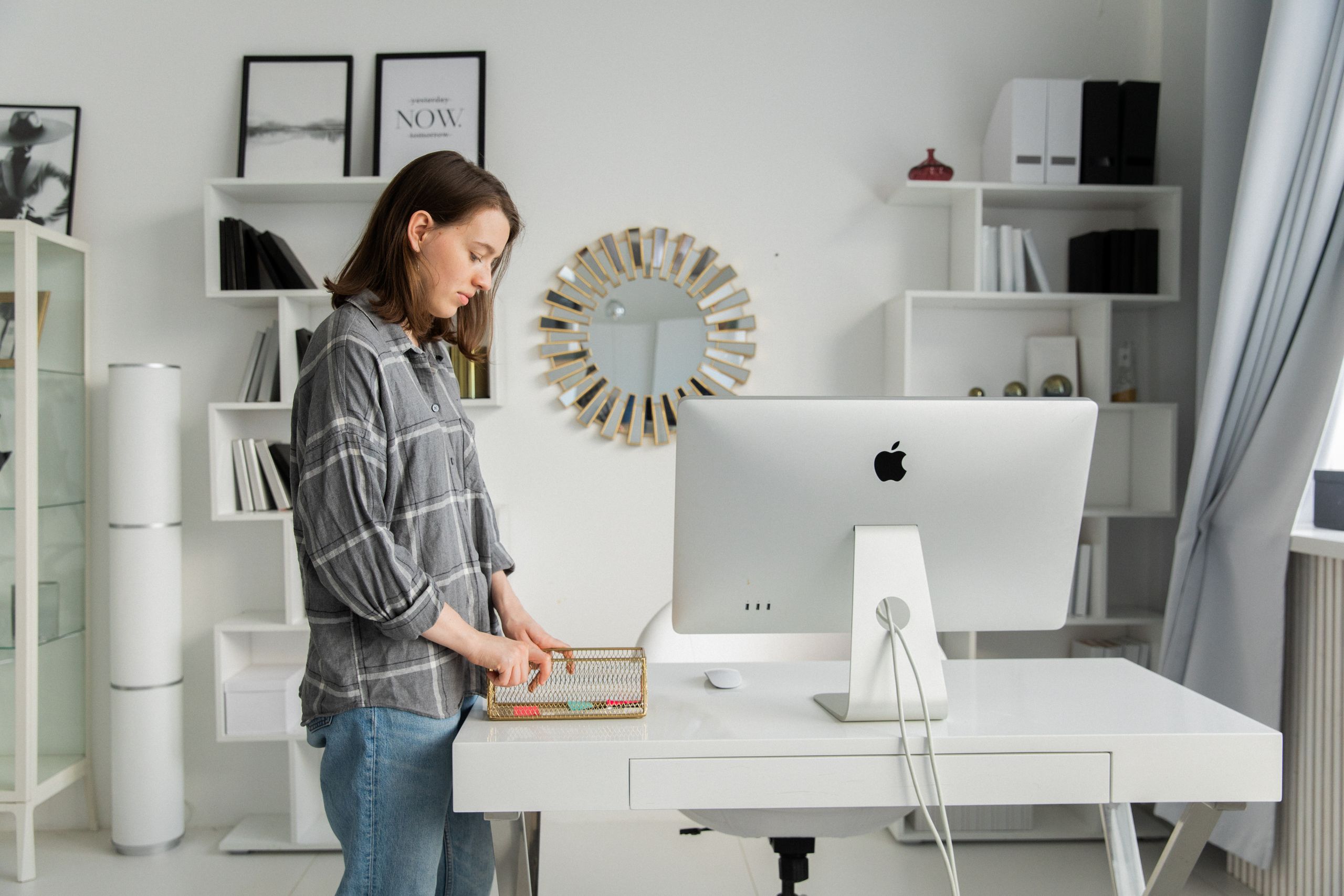 Adult woman organizing her desk with a desktop in a modern, stylish office with shelves and decor.