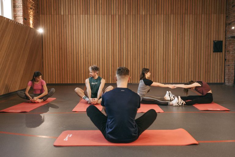 A group of adults practicing yoga and stretching on mats in a wooden panelled room.