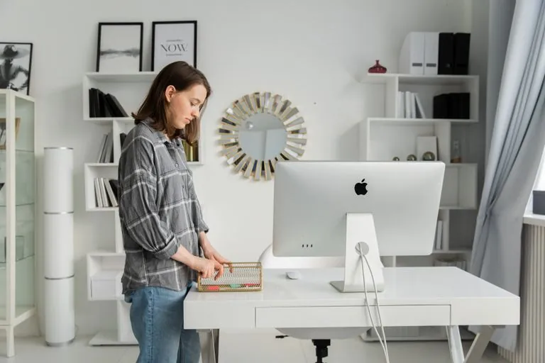 Adult woman organizing her desk with a&nbsp;desktop in a&nbsp;modern, stylish office with shelves and decor.